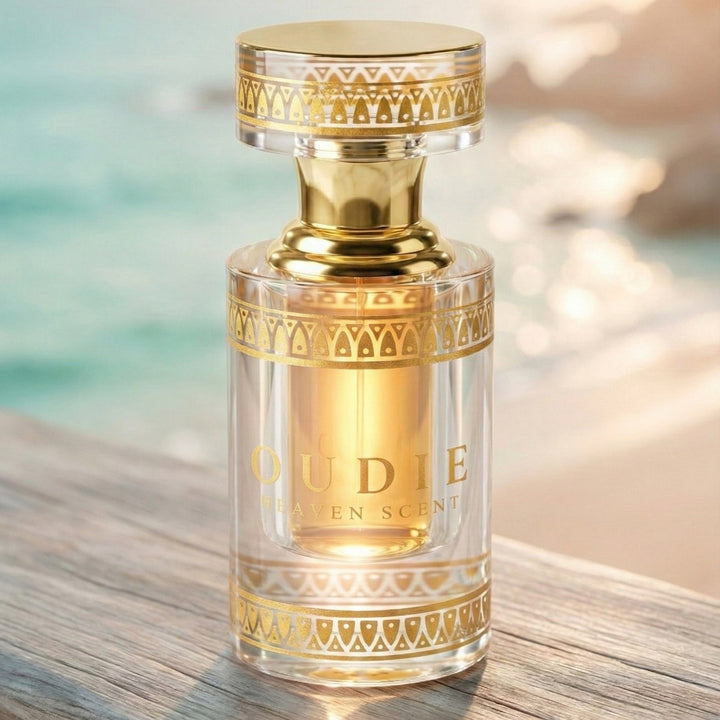 Gold and clear perfume bottle labeled 'Oudie' on a wooden surface with a blurred background